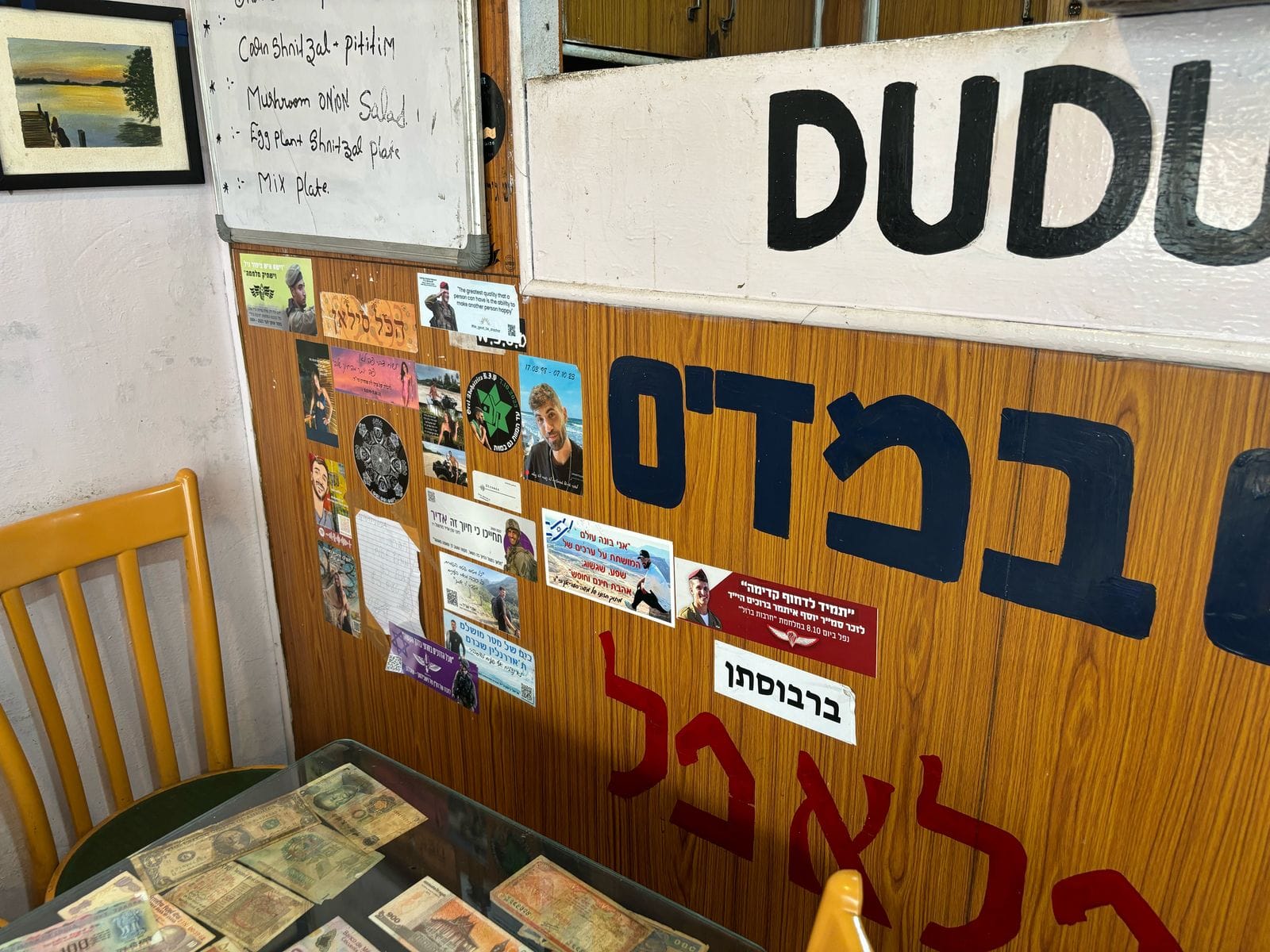 A wooden wall in a restaurant is covered in Hebrew letters and Hebrew stickers.